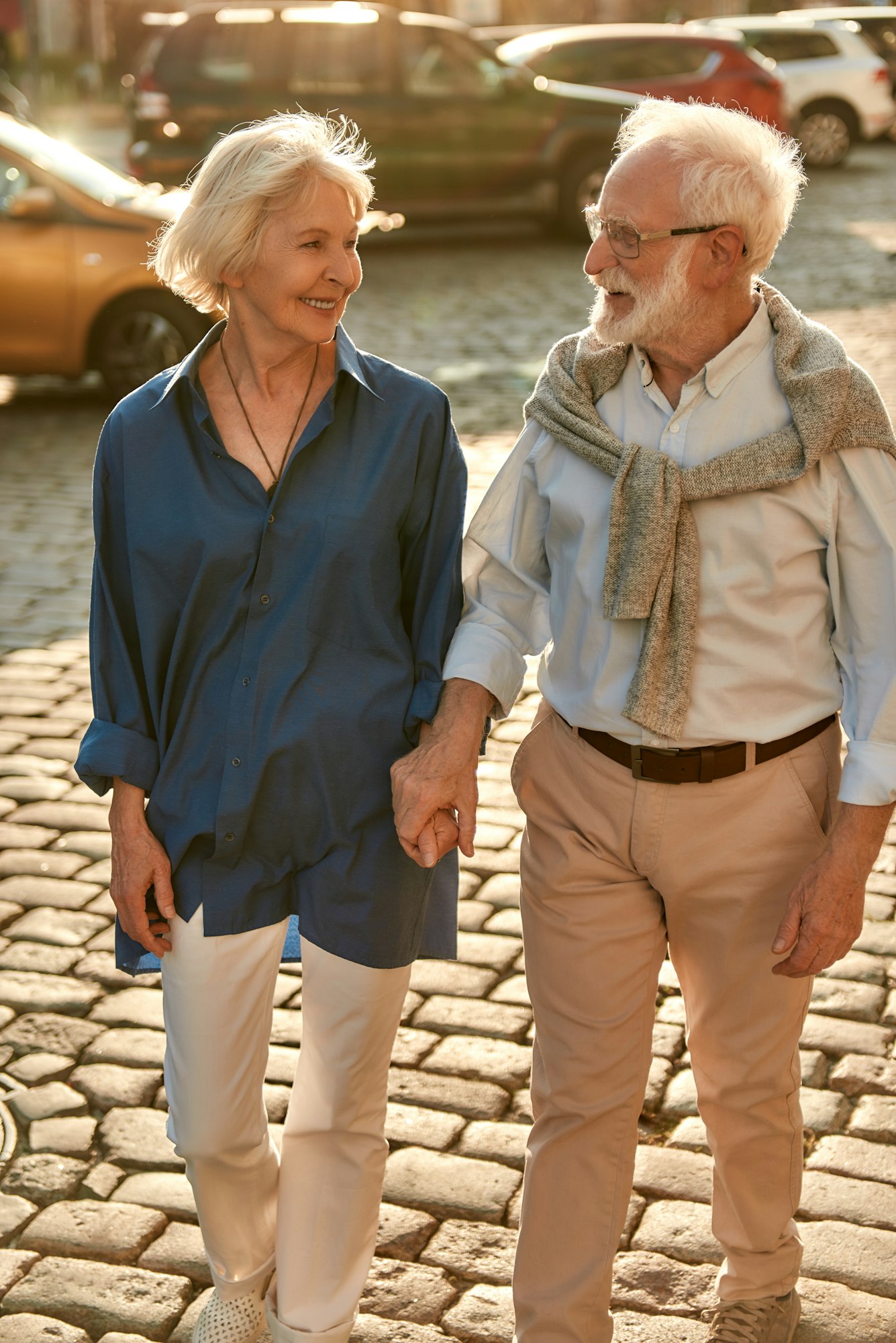 Active weekend. Elderly couple holding hands and looking to each other with smile while walking