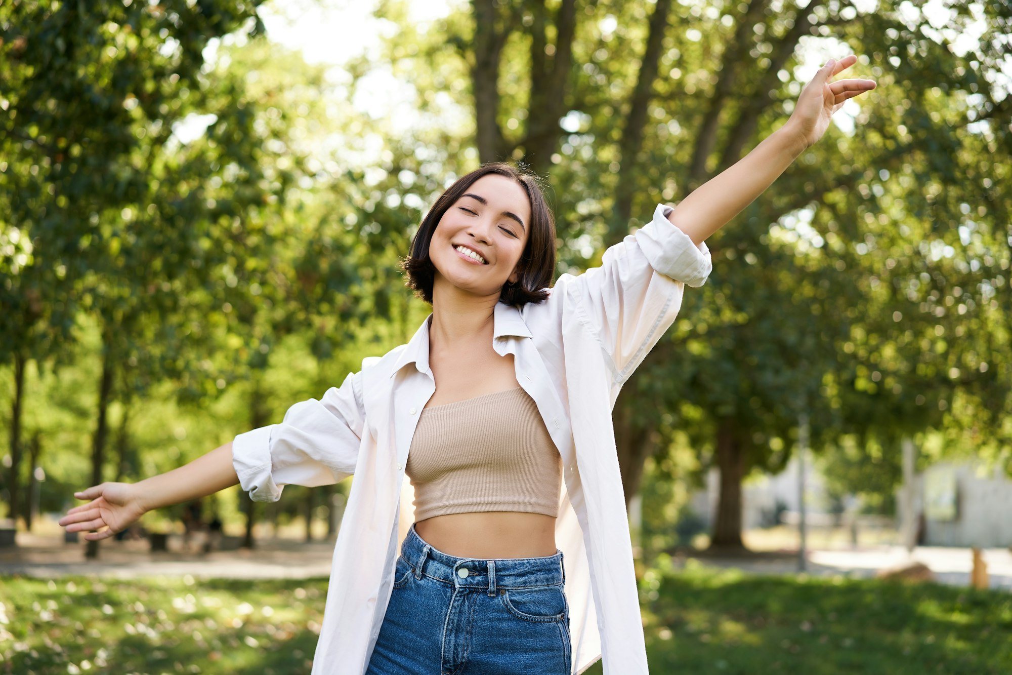 Carefree woman dancing and walking in park with hands lifted up high, smiling happily. Lifestyle